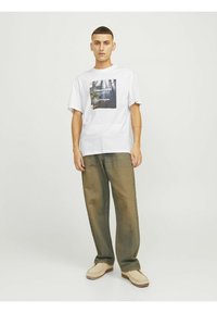 Hvid kortærmet t-shirt med grafisk print, parret med løsere olivengrønne bukser og beige slip-on fodtøj.