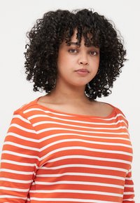 Gestreiftes Langarmshirt mit kräftigen orangefarbenen und weißen Linien, aus weichem Stoff mit einem breiten, schulterfreien Ausschnitt und lockerer Passform.