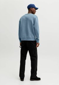 Sudadera azul claro con puños y dobladillo acanalados, combinada con pantalones cargo negros con bolsillos laterales. Un gorro azul completa el conjunto.