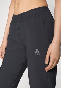 Crne sportske hlače s elastičnim pojasom, s diskretnim Odlo logotipom i bočnim džepom s patentnim zatvaračem za sigurno pohranjivanje.