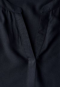 Blouse noire avec un col en V, présentant de subtiles plis et des coutures visibles. Tissu lisse avec une finition mate. Pas de motifs ni d'ornements.