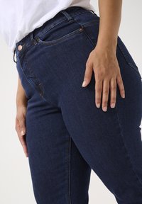 High-waisted dark blue jeans made of denim, featuring five pockets, copper rivets, and subtle contrast stitching details.