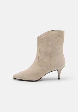 Stivaletto alla caviglia in camoscio beige con punta appuntita e tacco inclinato. Texture liscia, design minimalista con cuciture laterali.