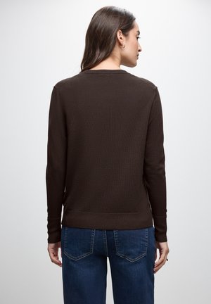 Pull en maille marron avec des manches longues, ourlet côtelé et texture lisse, porté sur un jean en denim bleu, vu de dos.