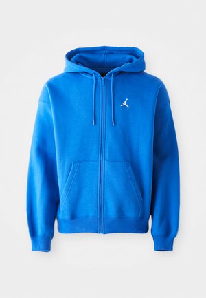 Blauwe rits-hoodie gemaakt van zacht materiaal, met een kangoeroezak, een trekkoordkap en een witte Jordan-logo op de linkerkant van de borst.