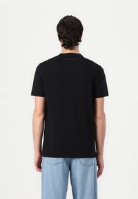 Svart bomull T-skjorte med rund hals, korte ermer og subtil merking på baksiden. Kombinert med lyseblå denimbukser.