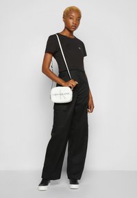 T-shirt nera con logo sottile, abbinata a pantaloni cargo neri larghi. Accessoriata con una borsa a tracolla bianca con un accento logo.