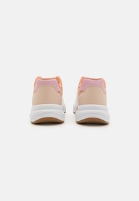 Tan and pink sneakers with a smooth material, rounded shape, padded collar, and white soles. Features textured accents and contrasting colors.
