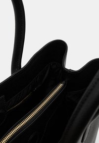 Borsa a tracolla in pelle nera con apertura superiore, che mostra un interno in raso e una tasca con zip dorata su un lato, caratterizzata da un esterno testurizzato.