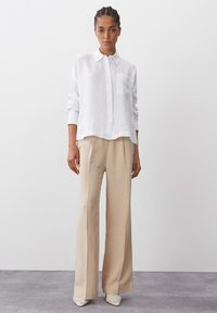 White linen button-up shirt with long sleeves and a chest pocket, paired with beige wide-leg trousers and patterned shoes. Minimalist design.