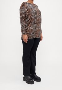 Långärmad topp med leopardmönster i brunt och svart, kombinerad med svarta rakbenbyxor och kraftiga svarta boots. Mjuk, strukturerad tyg.