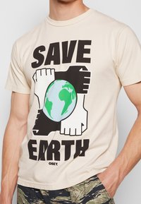 Muž v béžové košili s textem "SAVE EARTH", černé a bílé ruce tvořící čtverec kolem grafiky Země v zelené a modré barvě.