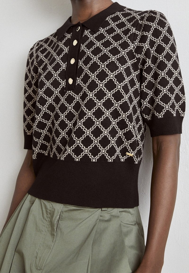 Sweter polo w ciemnym brązie z kremowym geometrycznym wzorem, z kołnierzykiem i listwą na cztery guziki, połączony z khaki spódnicą.