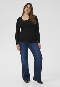 Black ribbed long-sleeve top with lace trim neckline, paired with flared dark blue jeans. Both garments feature a smooth texture and casual fit.