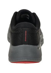 Scarpa sportiva nera con tomaia in tessuto testurizzato, collo imbottito e suola grigia ammortizzata. Presenta un marchio rosso sul tallone.