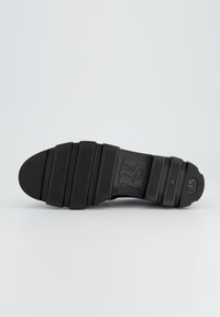 Schwarze Gummisohlen mit strukturierten Rillen, glatten Abschnitten und einem Logodetail. Flache Form, die für Traktion und Komfort ausgelegt ist.