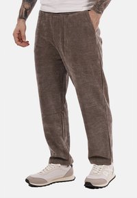 Pantaloni in corduroy di un tono marrone tenue, con una superficie testurizzata, tasche laterali e una vestibilità rilassata, abbinati a sneaker grigie e bianche.