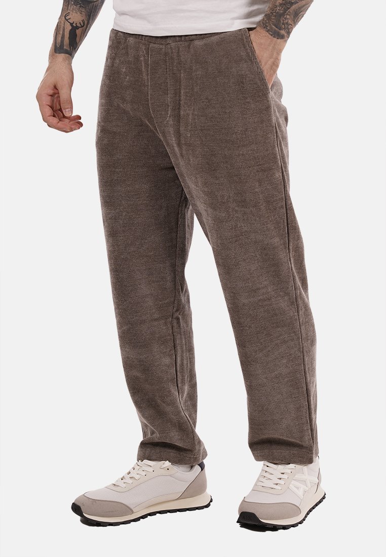 Pantaloni in corduroy di un tono marrone tenue, con una superficie testurizzata, tasche laterali e una vestibilità rilassata, abbinati a sneaker grigie e bianche.