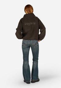 Tumehall fleece-jope, millel on üleskeeratud kaelus ja logo seljal, koos siniste flared teksadega, millel on detailne pitser õmblustes taskutel.