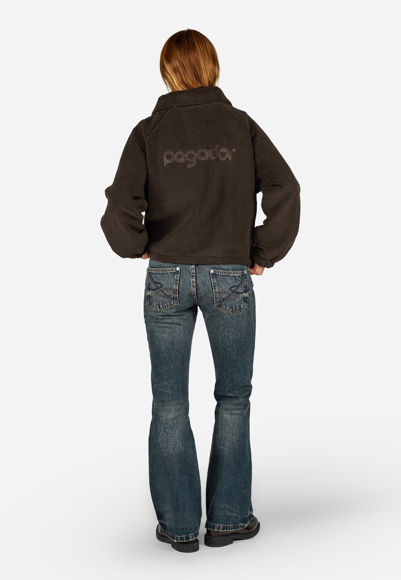 Tumehall fleece-jope, millel on üleskeeratud kaelus ja logo seljal, koos siniste flared teksadega, millel on detailne pitser õmblustes taskutel.