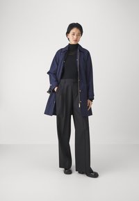 Palton bleumarin cu elemente aurii, purtat peste un pulover negru cu guler înalt și pantaloni negri cu picioare largi; pantofi negri fără toc completează ținuta.