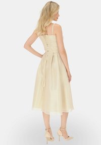 Beżowa satynowa sukienka z dopasowaną górą, sznurówką z tyłu i zwiewnym, długości do kolan dołem. Połączona z jasnymi szpilkami.
