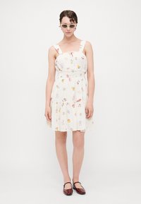 Vestido blanco de longitud hasta la rodilla con estampado floral, tirantes anchos y cintura fruncida. Un par de zapatos cerrados burdeos complementan el conjunto.