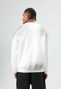 Witte sweatshirt met een kleurverloop dat naar grijs vervaagt aan de onderkant, een ontspannen pasvorm, lange mouwen, geribbelde manchetten en zoom. Draagt over een zwarte broek.