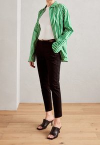 Grön- och vitrandig oversized skjorta, vit topp, svarta slim-fit byxor, och svarta öppna klackskor på en trägolv.