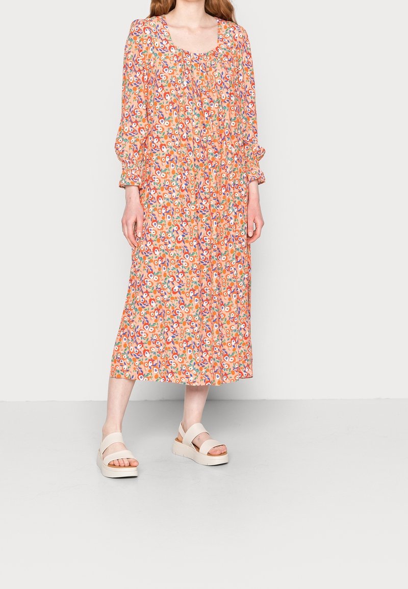Robe maxi à imprimé floral orange, avec un décolleté carré et des manches froncées, assortie à des sandales plates-formes blanches épaisses.