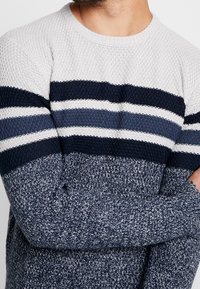 Navy and light gray striped knitted sweater with a textured finish and ribbed crew neckline, featuring three horizontal stripe bands.