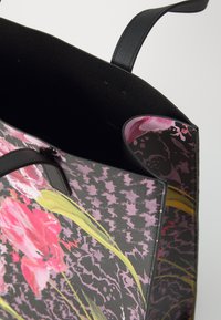 Bloemen tote bag met een zwarte basis en roze en groene bloemenpatronen. Voorzien van zwarte handvatten en een gladde textuur. Ruime binnenkant.