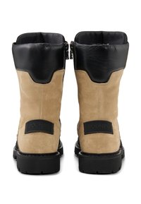 Boty mají hnědý svršek z semiše s kontrastním černým koženým lemem. Mají pevnou černou gumovou podrážku a logo na zadní straně.