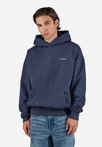 Navy blauwe hoodie van katoen, met een voorzak en ribgebreide boorden. Subtiele logo borduring op de borst.