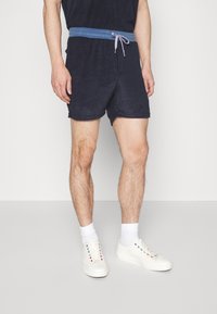 Shorts en tissu éponge bleu marine avec une ceinture à cordon bleu clair. Associés à des chaussures et des chaussettes blanches, mettant en valeur une coupe décontractée et une texture agréable.