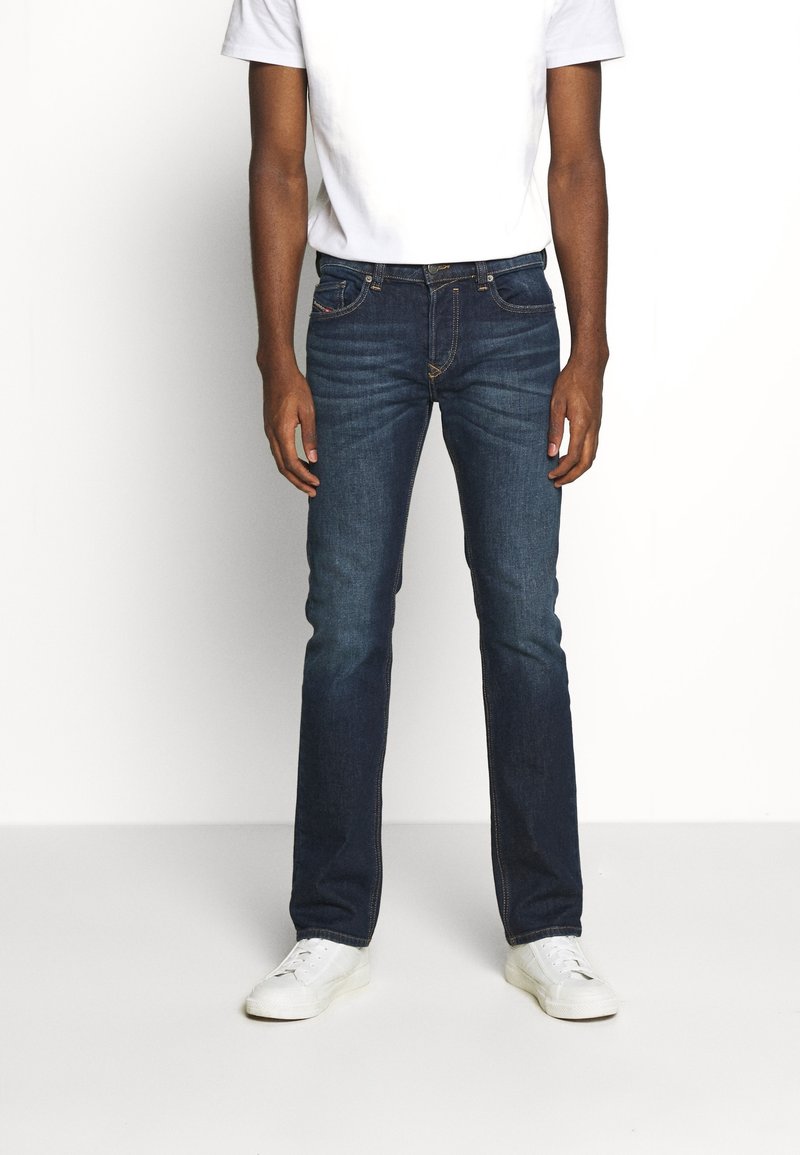 Mörkblå denimjeans med klassisk passform, som har fem fickor och en subtil sömdekoration. Kombineras med en enkel vit t-shirt och vita sneakers.
