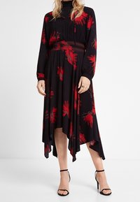 Musta mekko punaisilla kukkakuoseilla, smockattu vyötärö, pitkät hihat, epäsymmetrinen helma ja pehmeä kangas. Yhdistetty mustiin ohuisiin korkokenkiin.