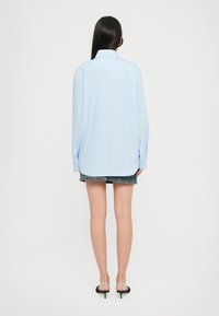 Camicia azzurra a maniche lunghe con colletto, orlo arrotondato e polsini abbottonati, abbinata a una gonna di jeans. Texture liscia.