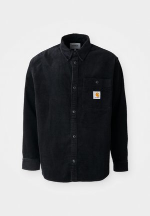 Camisa de corduroy negra de manga larga con botones en la parte delantera, bolsillo en el pecho que presenta un pequeño parche del logo de Carhartt en naranja.