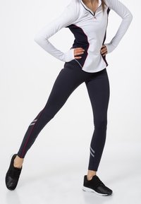 Zestaw odzieży sportowej składający się z białej i granatowej koszulki z długim rękawem z czerwonymi akcentami oraz granatowych legginsów z szarymi paskami i eleganckim designem.