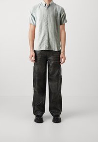 Korte mouwen, button-up blouse in lichtblauw met verticale strepen, gecombineerd met hooggebonden zwarte leren broeken en stevige zwarte schoenen.