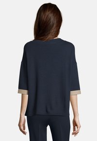 Marinblå ribbstickad tröja med breda, korta ärmar och cuffs med guld-accent. Lättviktig, avslappnad passform med rund halsringning.