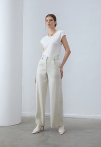 Witte fitted T-shirt gecombineerd met hooggewaisted, lichtbeige wijde broek met zijzakken en puntige, textuurgegeven crèmekleurige enkellaarsjes.
