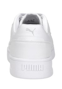 Zapatillas blancas con parte superior de cuero suave, cuello acolchado y logo grabado de "PUMA" en el talón. Suela de goma plana.