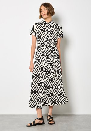 Robe maxi à motifs noir et blanc avec un col, des manches courtes et une taille nouée. Présente des formes de losange et un design fluide.