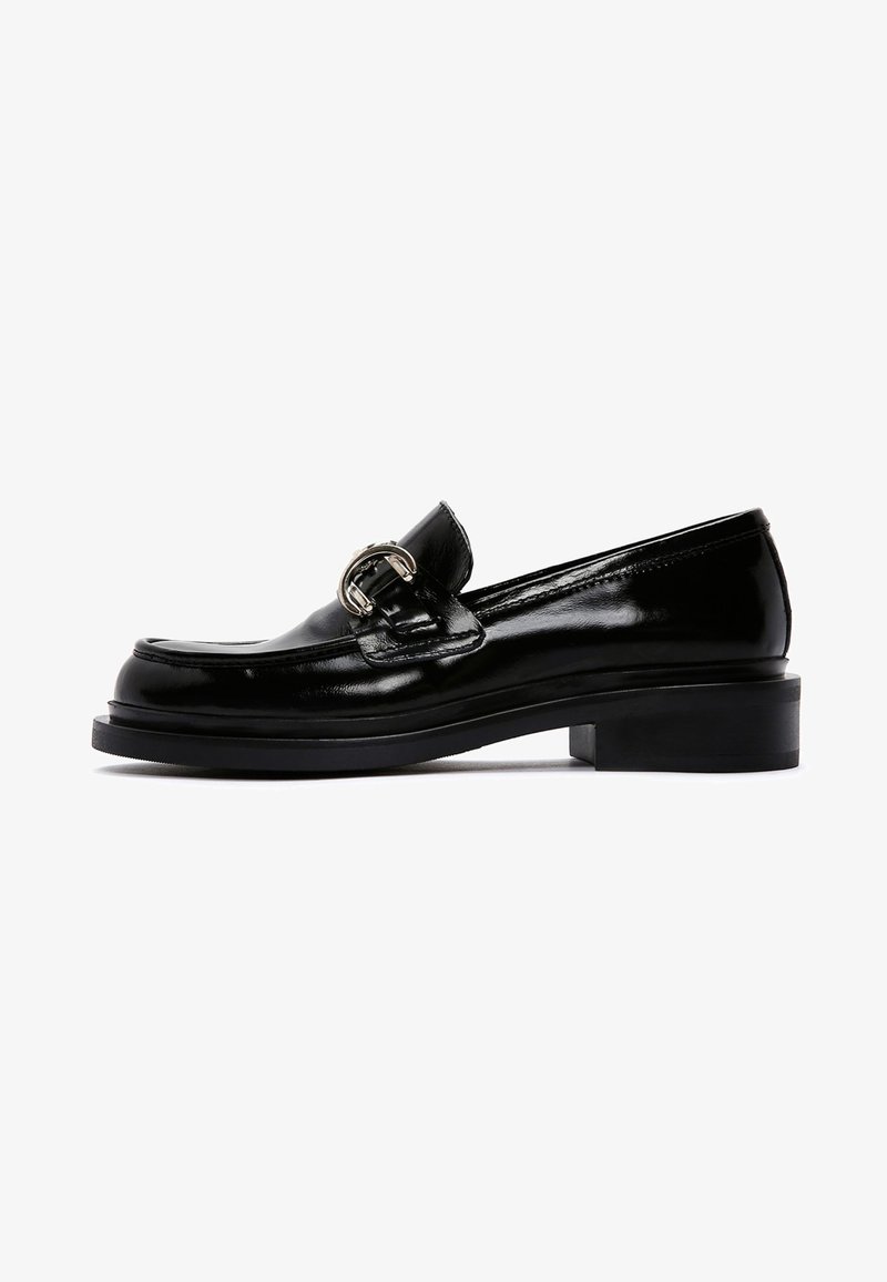 Mocassin en cuir verni noir avec un bout rond, un petit talon carré et une boucle en argent décorative sur le cou-de-pied. Texture lisse.