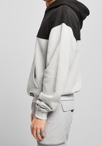 Sweat à capuche gris avec partie supérieure noire. Comprend une poche avant, des poignets côtelés et une capuche réglable avec cordelette. Design simple.