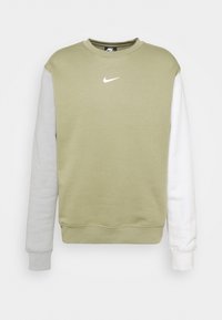 Nike-tröja med ljus olivgrön kropp, ljusgrå vänster ärm, vit höger ärm och vit Nike-logga på bröstet.