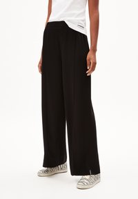 Pantalons noirs à large jambe en tissu lisse, avec une taille haute et un design plissé. Associés à des baskets à imprimé zèbre noir et blanc.