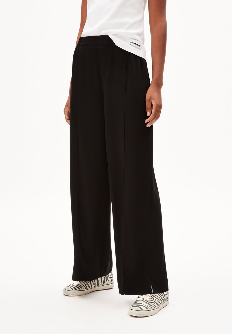 Pantalons noirs à large jambe en tissu lisse, avec une taille haute et un design plissé. Associés à des baskets à imprimé zèbre noir et blanc.